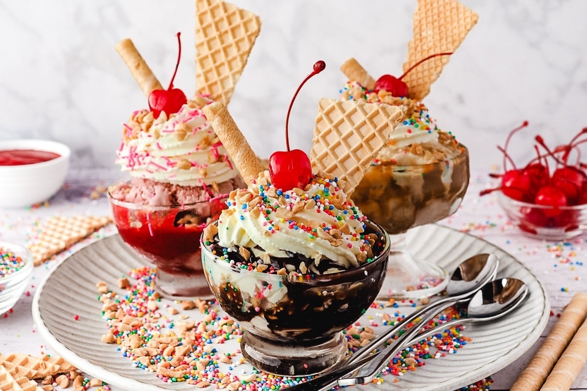 Three ice cream sundaes on a plate with sprinkles.