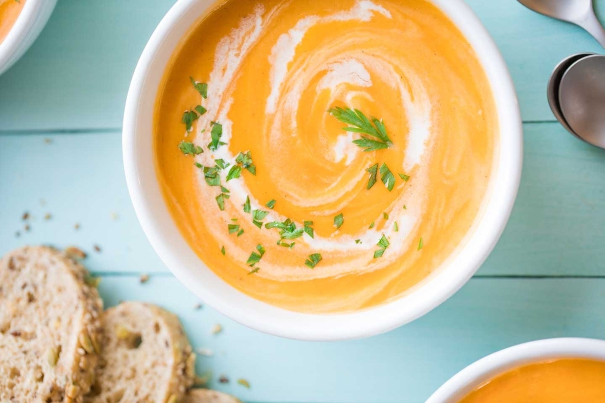 Three bowls of carrot soup on a wooden table.