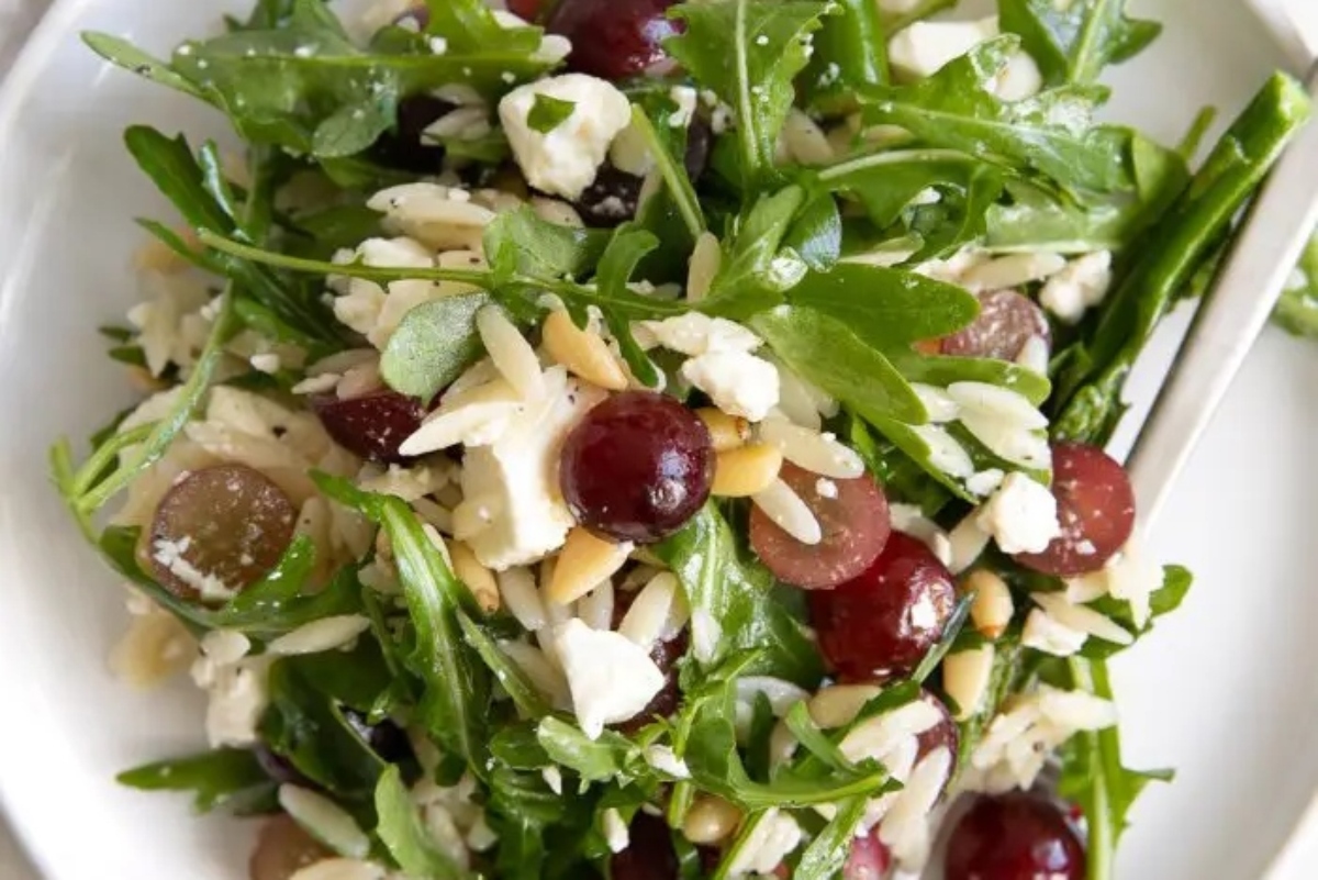 A plate with grapes, arugula and a fork.