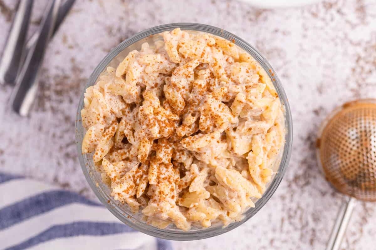 Orzo pudding in a glass bowl next to a spoon.