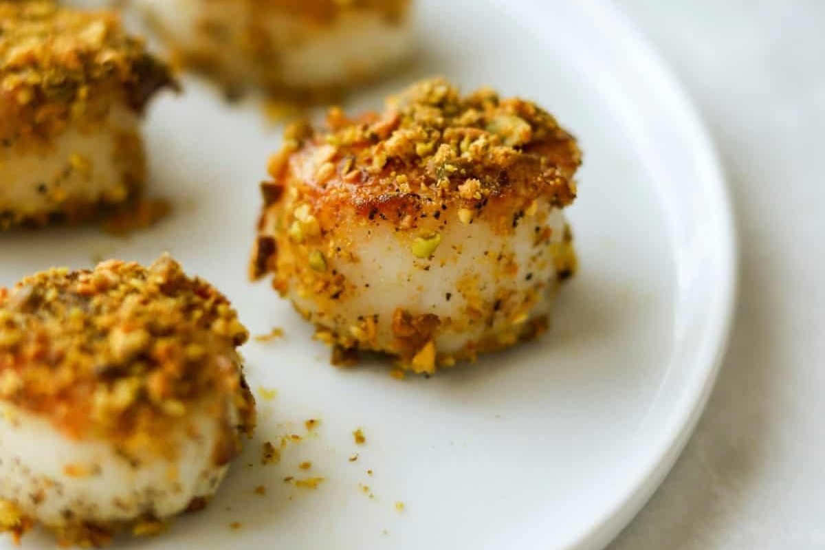 Scallops with pistachios on a white plate.