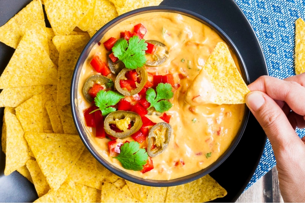 A person is dipping a tortilla into a bowl of mexican dip.