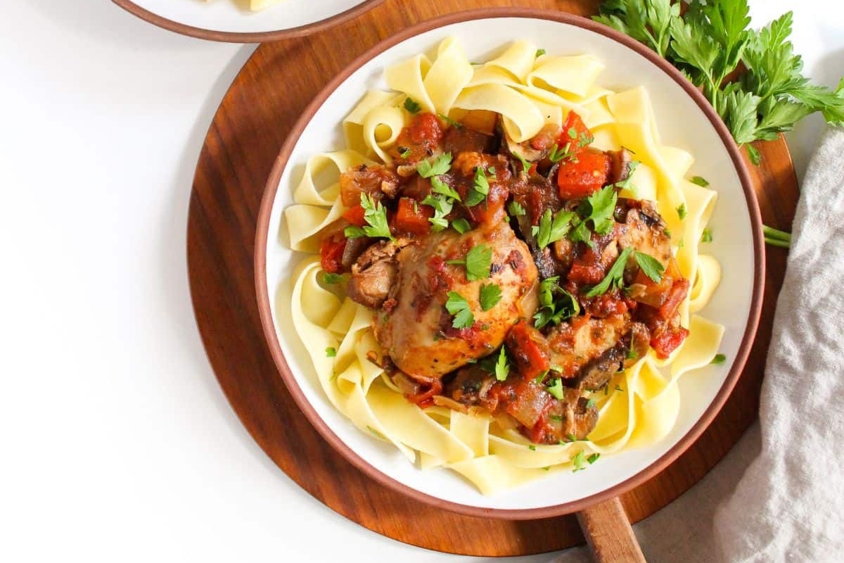 A plate of pasta with chicken and tomato sauce on a wooden cutting board.