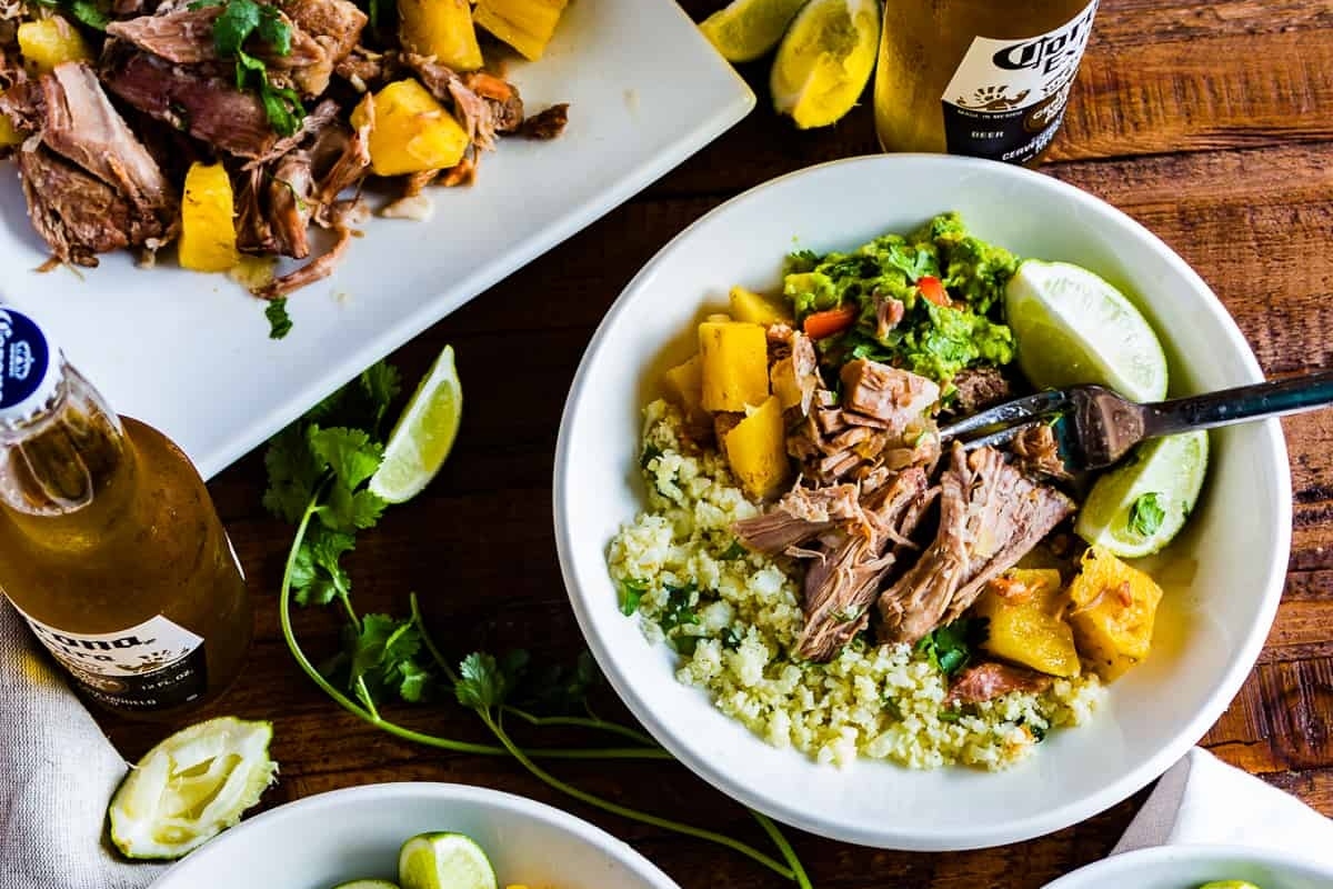 A bowl of pulled pork with rice and pineapple on a wooden table.