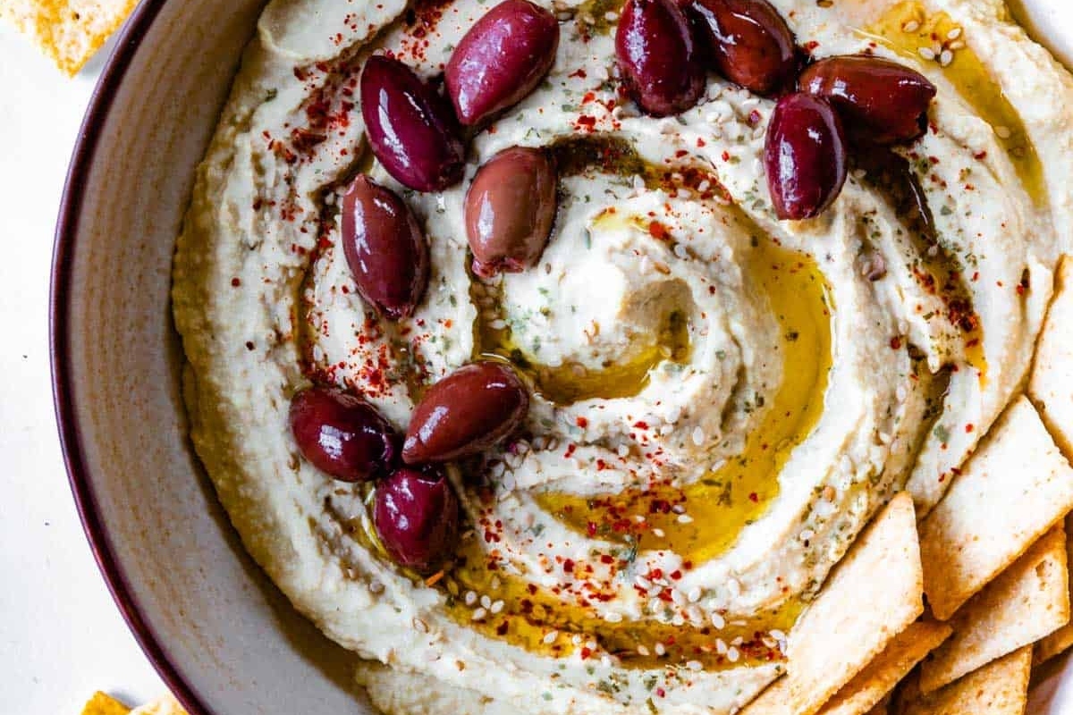 A bowl of hummus with olives and crackers.