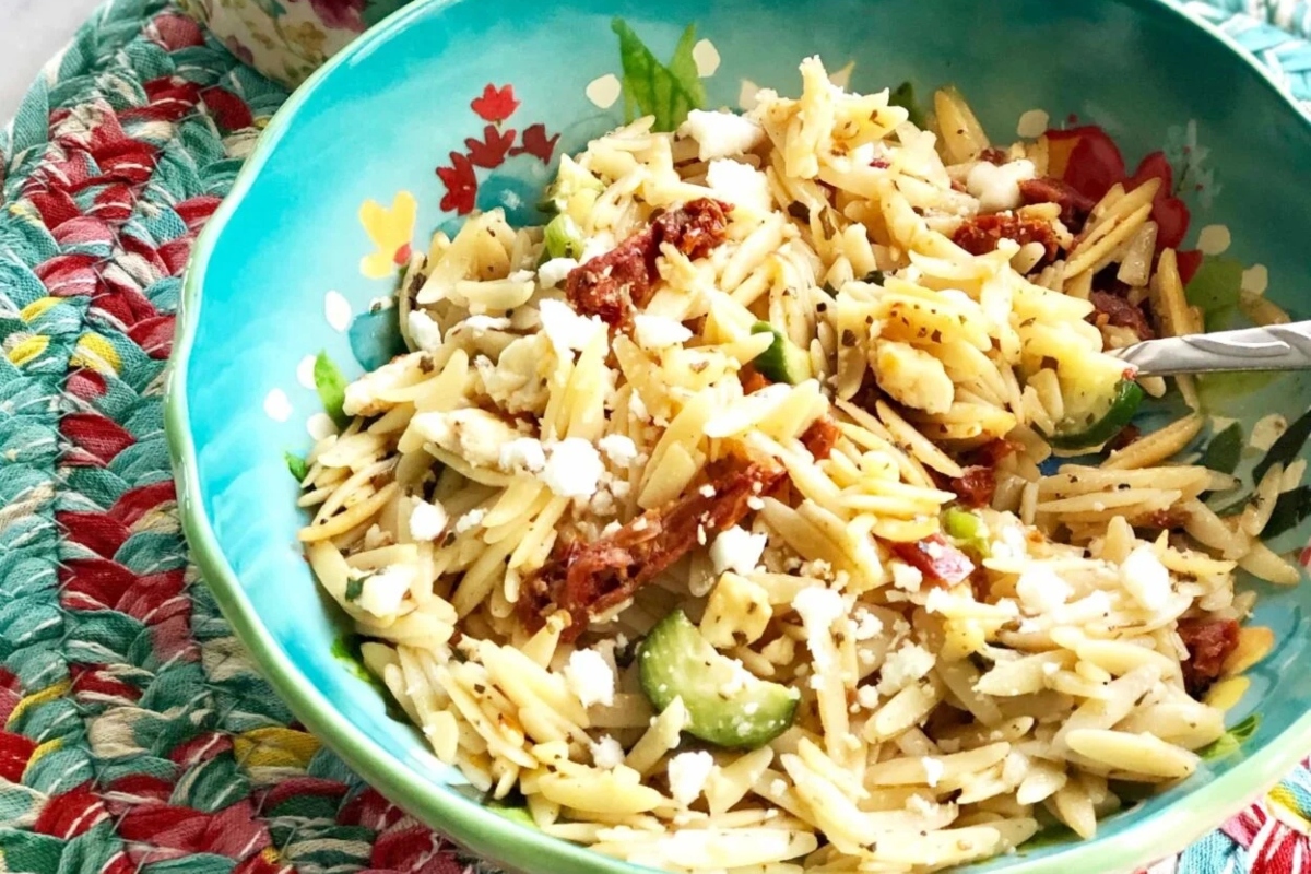 A bowl of pasta salad with tomatoes and olives.