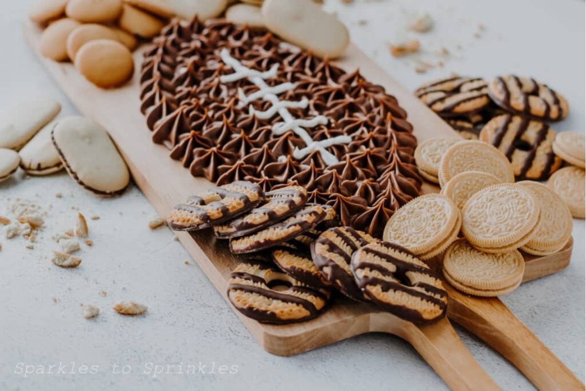 A wooden cutting board with cookies and a football on it.