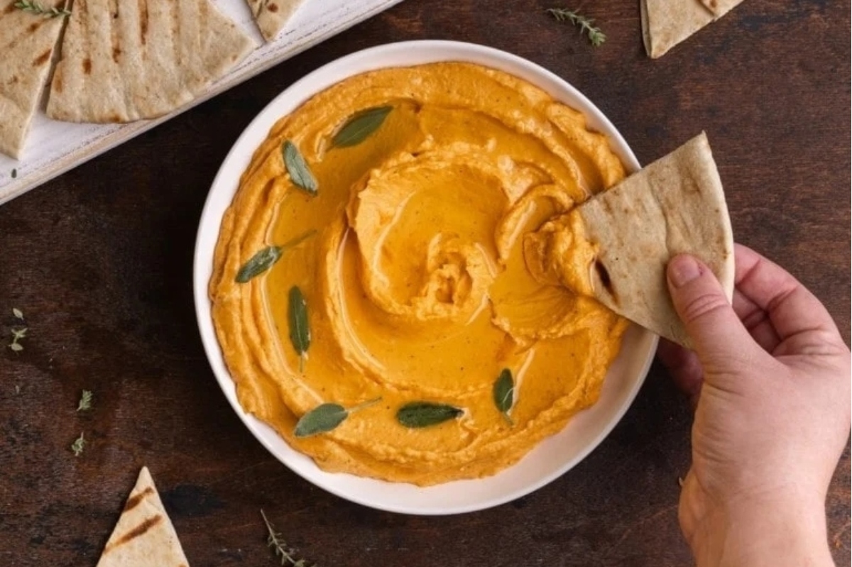 A bowl of hummus with pita chips and sprigs of sage.