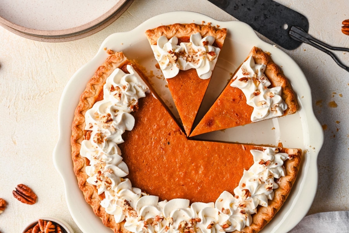 A pumpkin pie with whipped cream and pecans on a plate.
