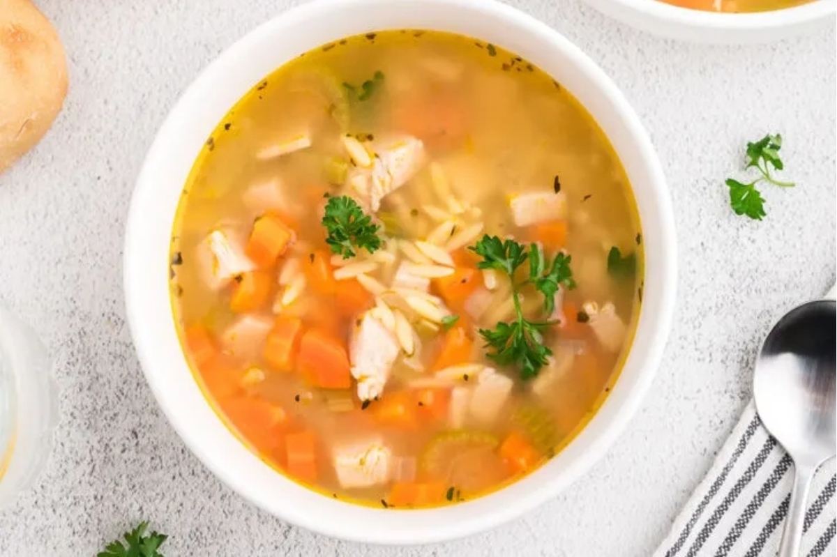 A bowl of chicken noodle soup with carrots and potatoes.