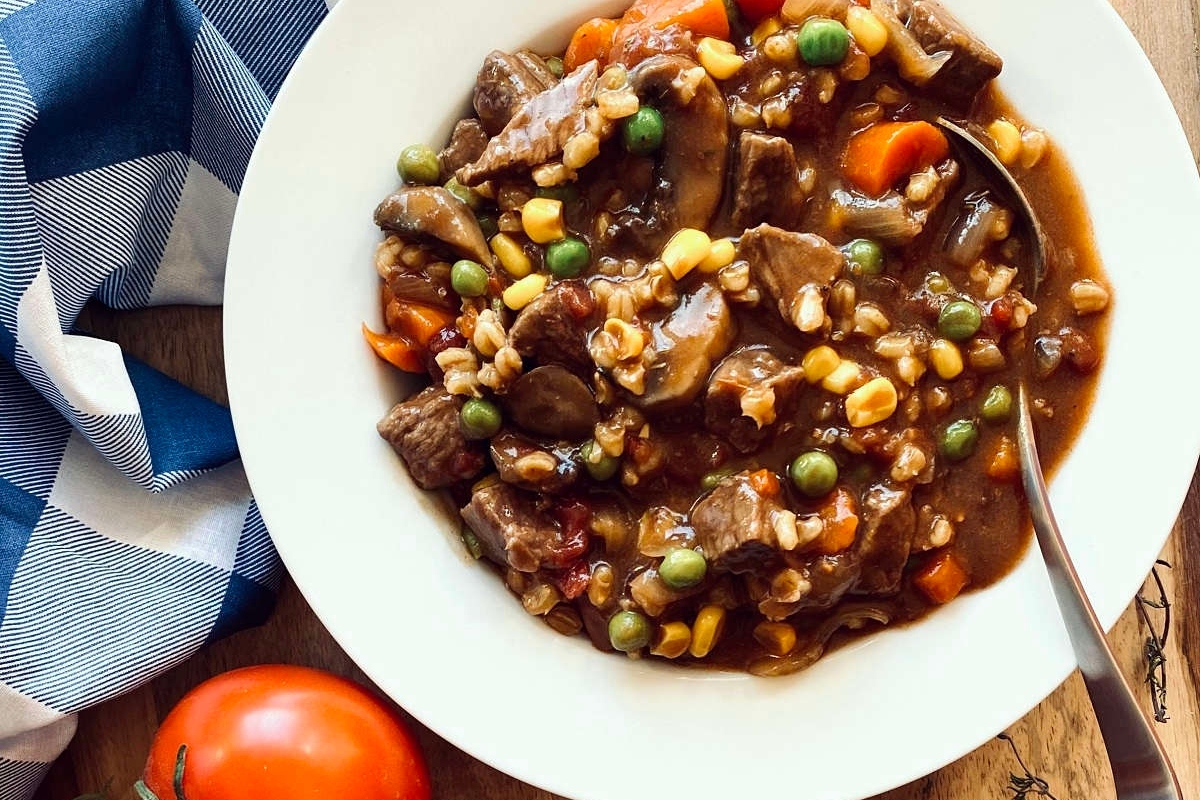 Beef stew in a white bowl with vegetables and a spoon.