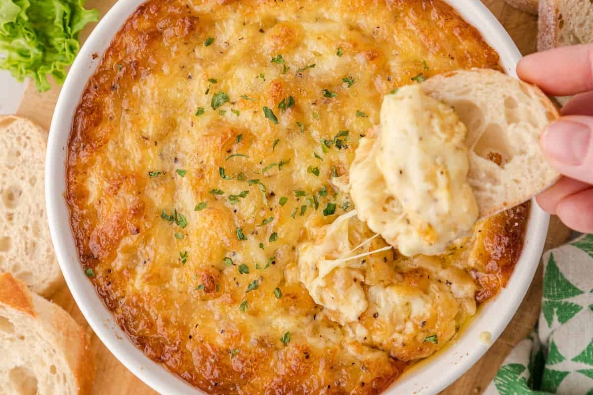 A person is dipping bread into a bowl of cheese dip.