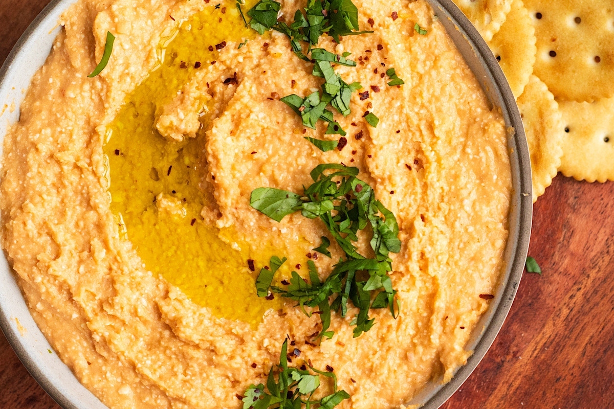 A bowl of hummus with crackers on a wooden table.
