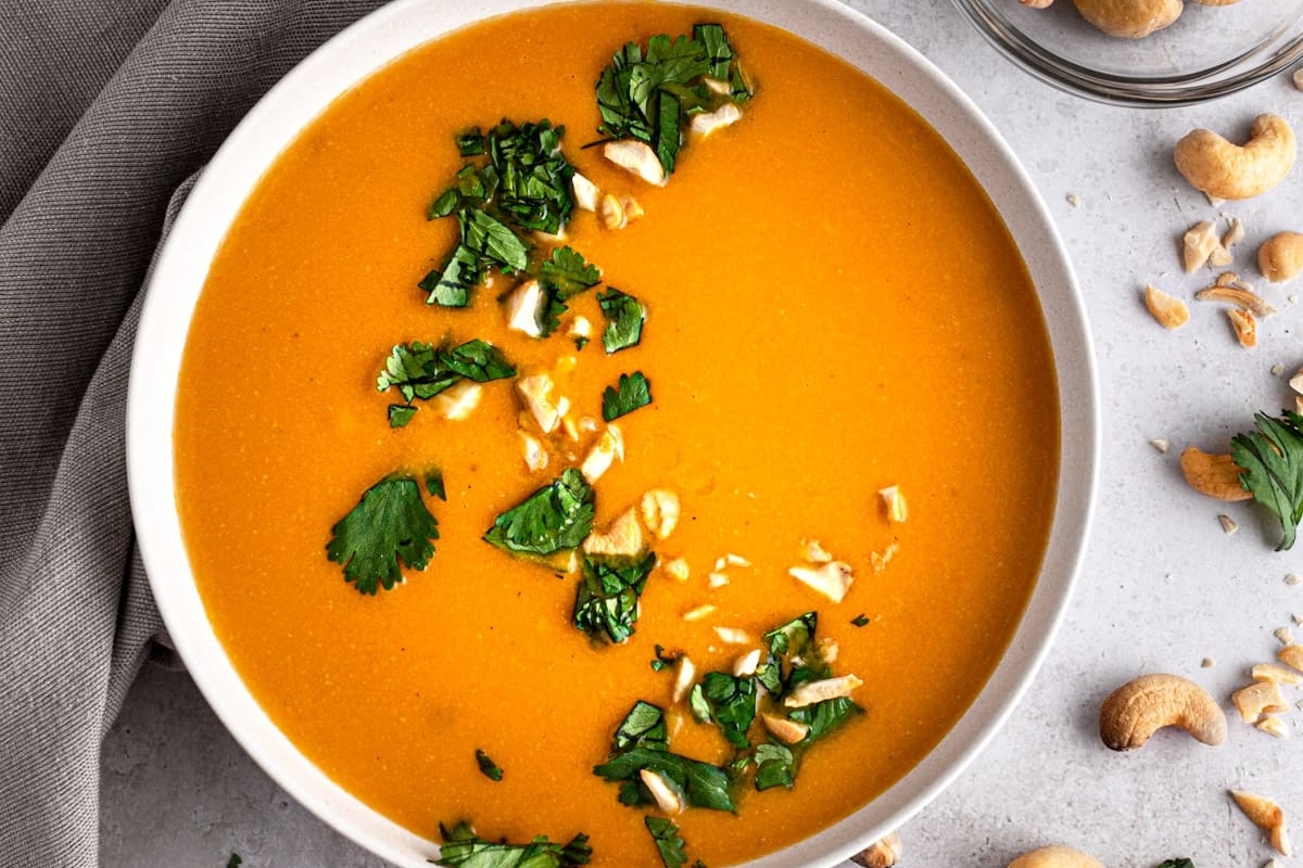 A bowl of carrot soup with cashews and parsley.