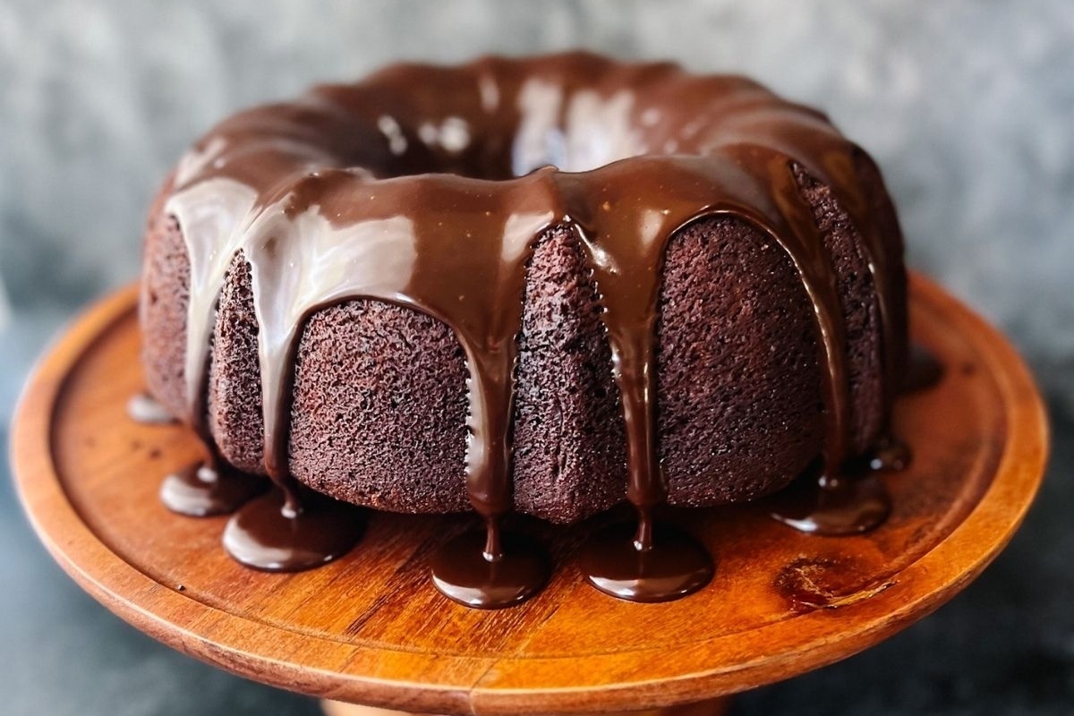 A chocolate bundt cake is sitting on a wooden plate.