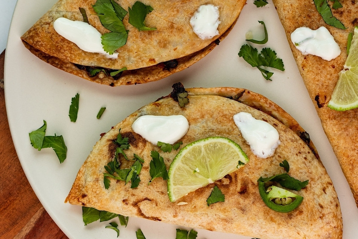 Three quesadillas on a plate with lime and sour cream.