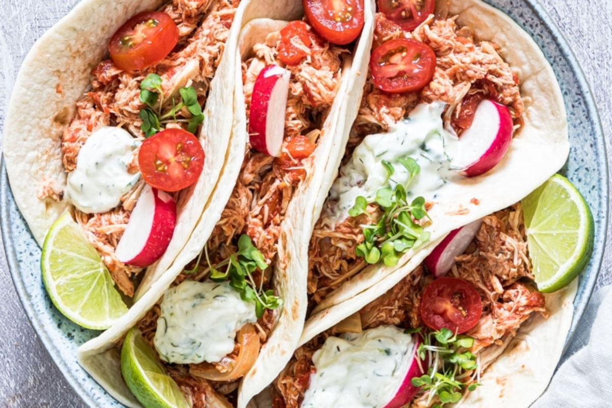 Shredded chicken tacos with sour cream and radishes on a plate.