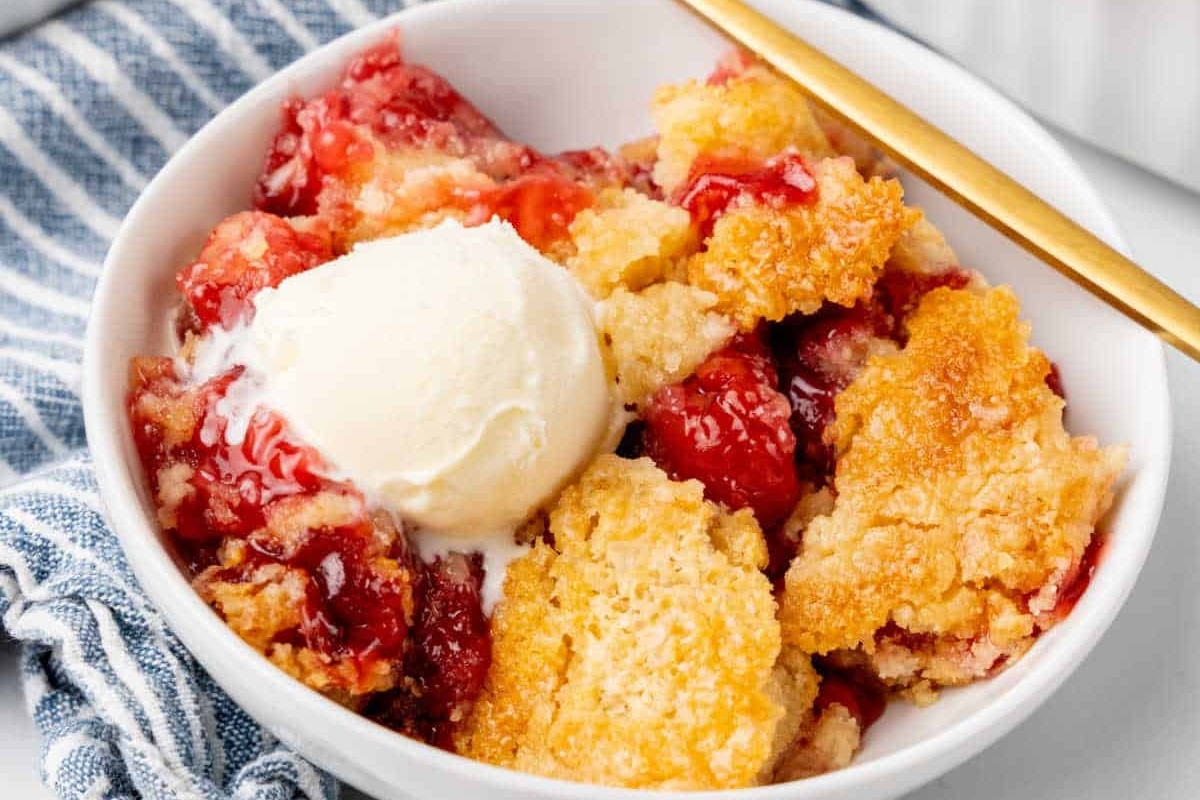 Strawberry cobbler in a white bowl with ice cream.