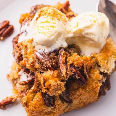 A plate with a slice of pecan cobbler with ice cream on it.