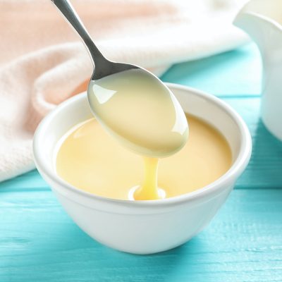 Spoon of pouring condensed milk over bowl on table. Dairy products