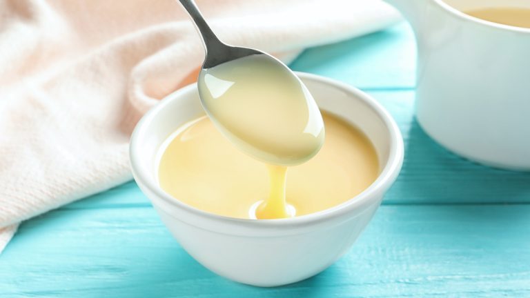 Spoon of pouring condensed milk over bowl on table. Dairy products