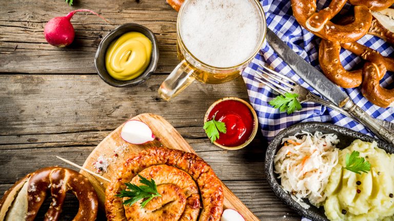 Oktoberfest food menu, bavarian sausages with pretzels, mashed potato, sauerkraut, beer bottle and mug old rustic wooden background