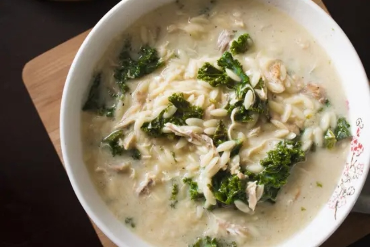 A bowl of chicken and kale soup on a wooden cutting board.