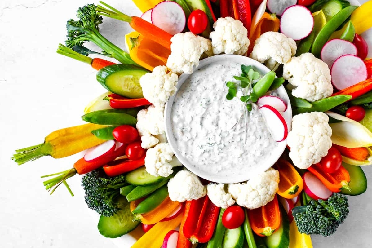 A bowl of dip surrounded by vegetables and radishes.