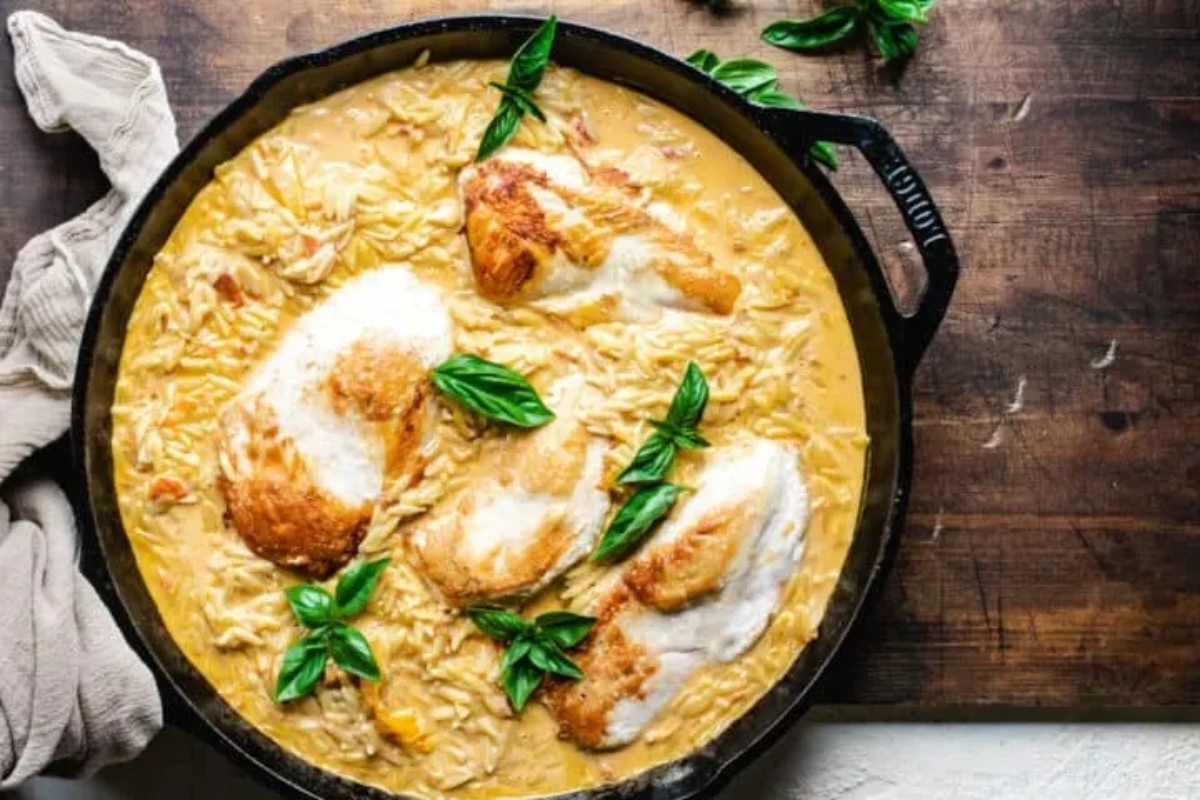 Chicken risotto in a skillet with basil leaves.