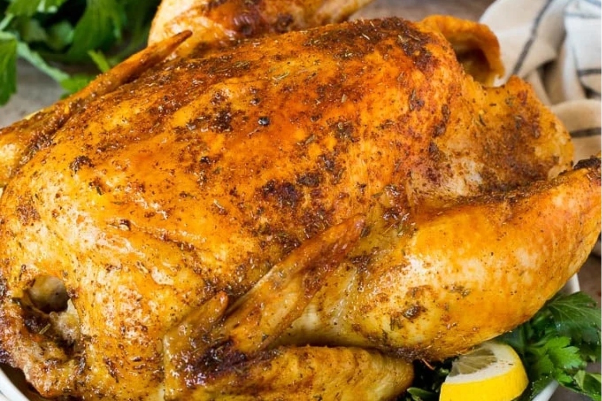 A roasted chicken on a plate with lemons and herbs.