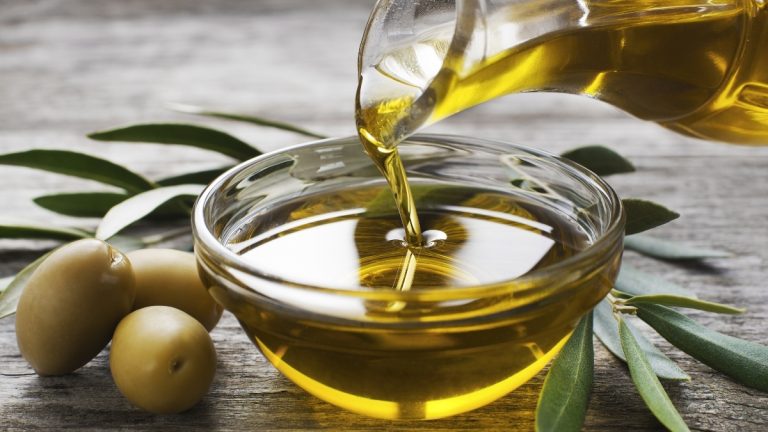 Bottle pouring virgin olive oil in a bowl close up
