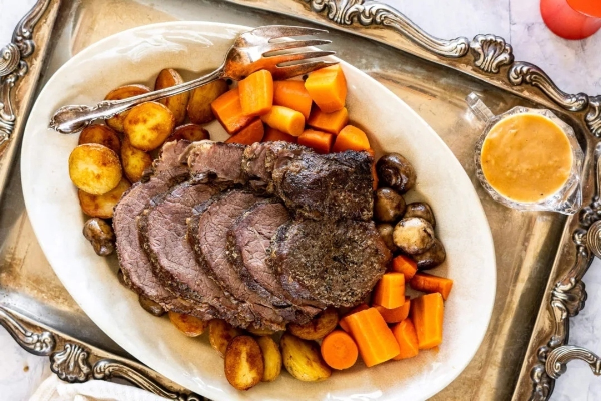 Roast beef with carrots and potatoes on a silver plate.