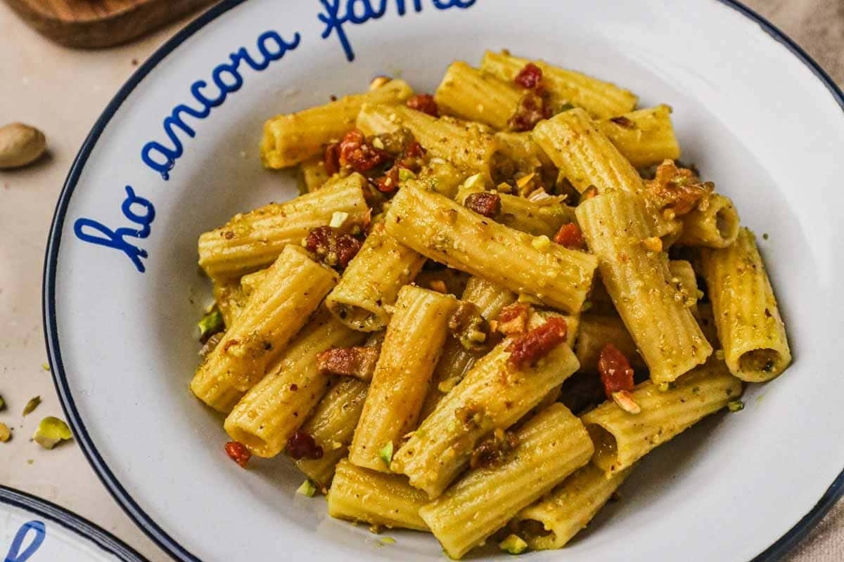 A bowl of pasta with tomatoes and pistachios.