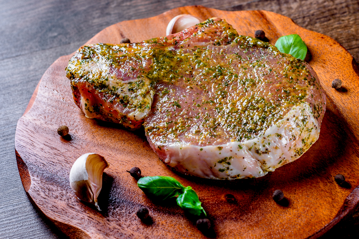 A raw pork chop on a wooden cutting board.