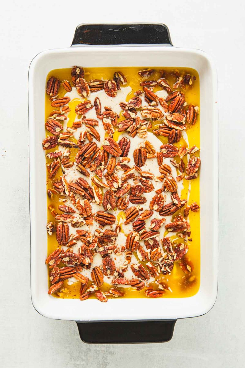 A white baking dish filled with raw pecan cobbler.