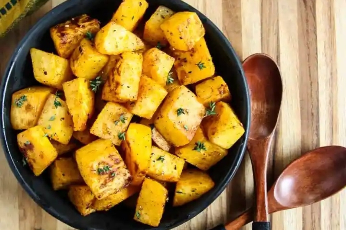Roasted sweet potatoes in a black bowl with wooden spoons.