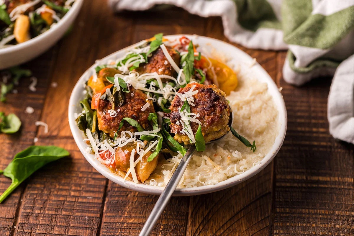A bowl of polenta and meatballs on a wooden table.