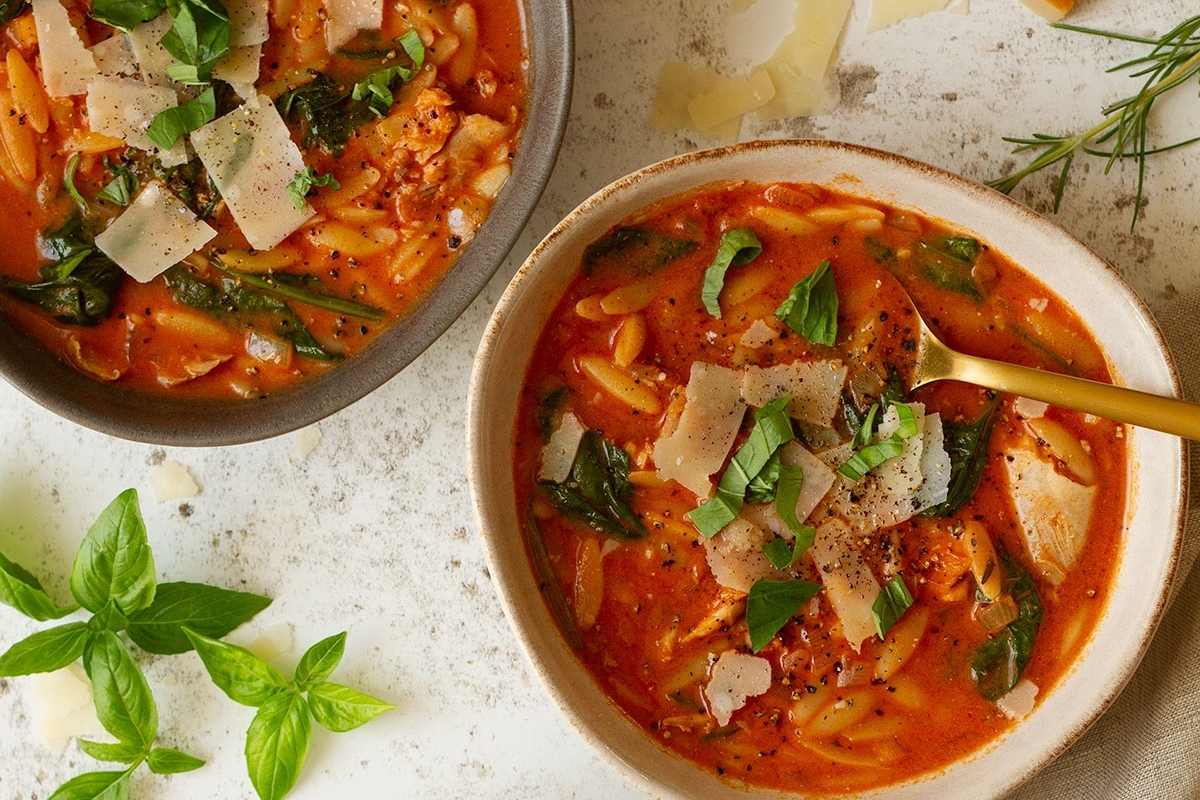 Two bowls of pasta with meat and spinach on a table.