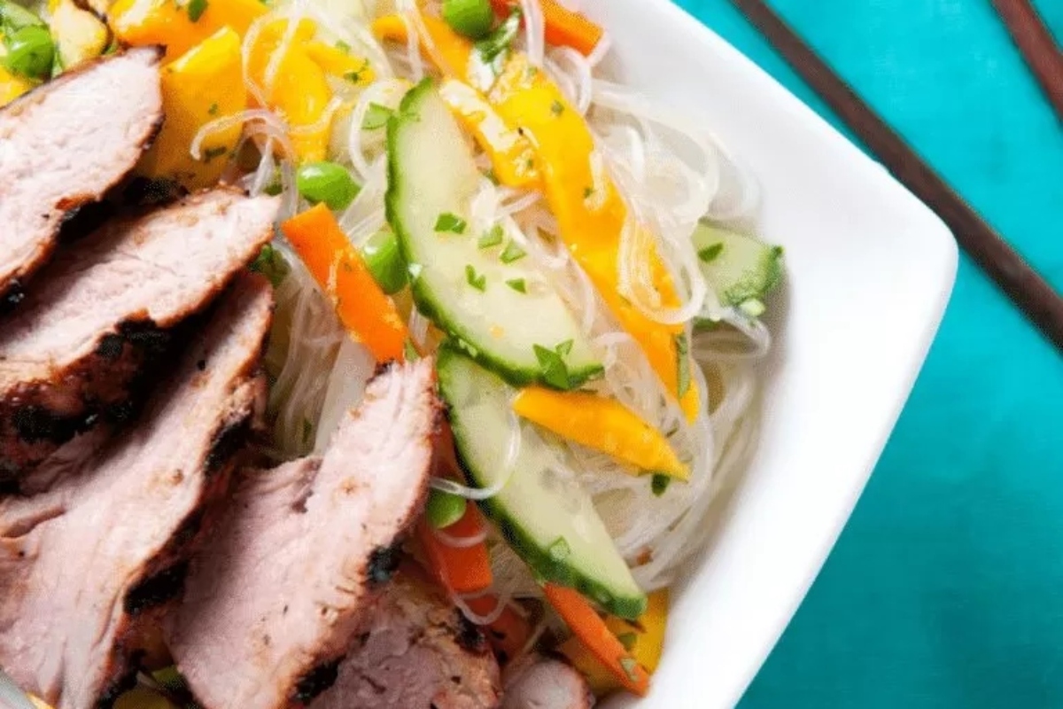 Asian pork noodle bowl with vegetables and chopsticks.