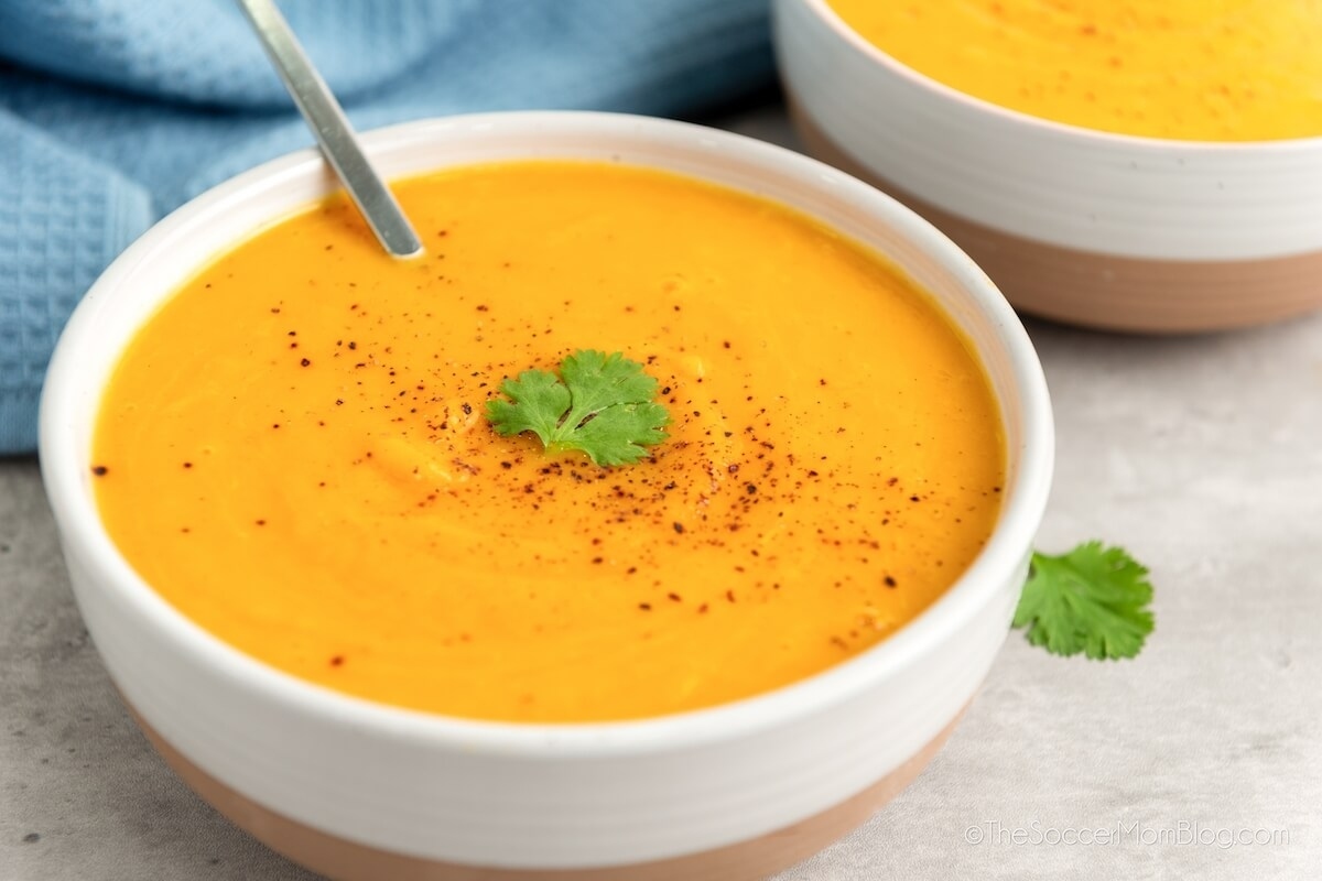 Two bowls of carrot soup with a spoon.