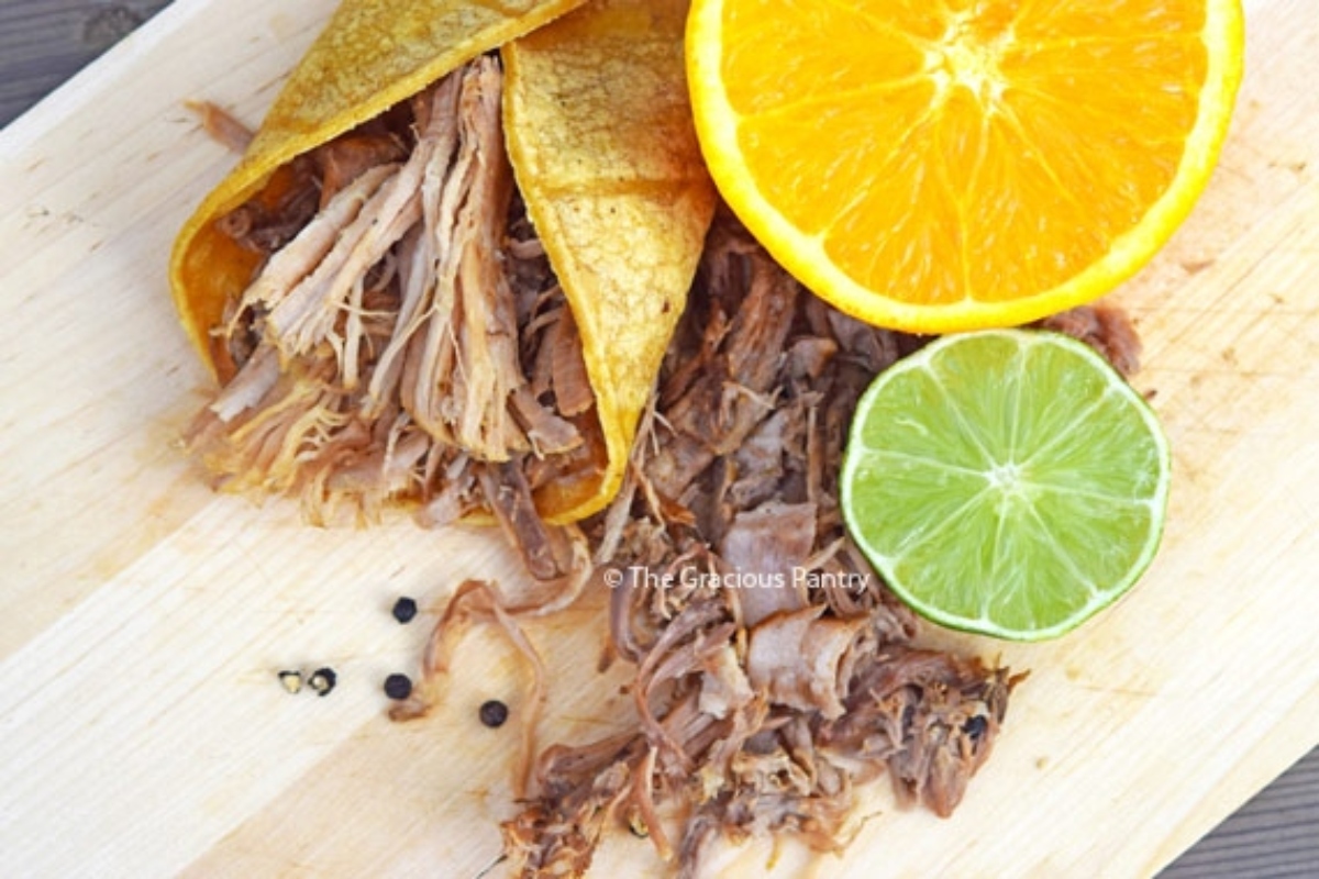 Pulled pork tacos on a cutting board with orange slices.