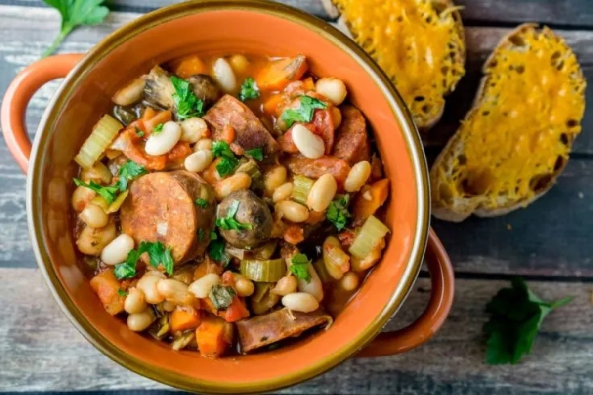 A bowl of bean and sausage stew on a wooden table.