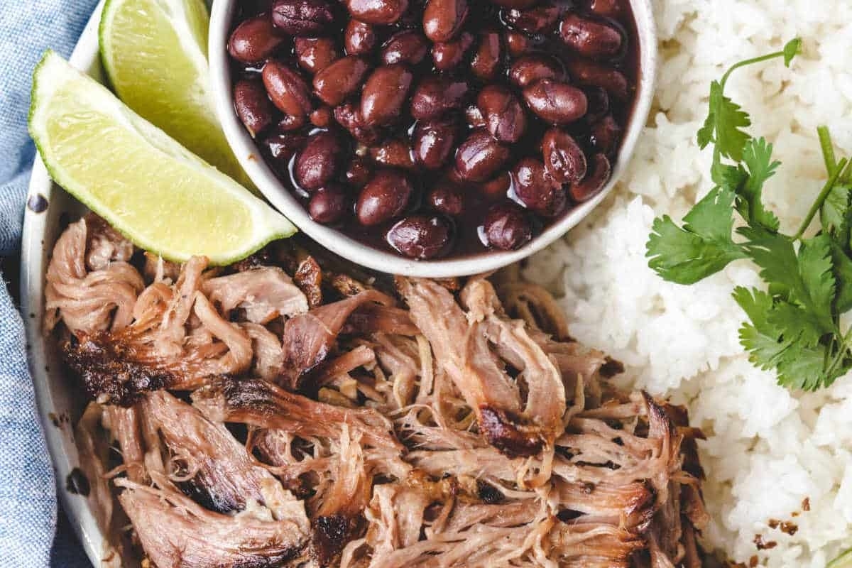 Pulled pork on a plate with rice and beans.