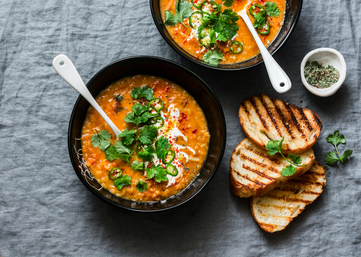 Curried red lentil tomato and coconut soup - delicious vegetarian food on grey background, top view. Flat lay served healthy lunch