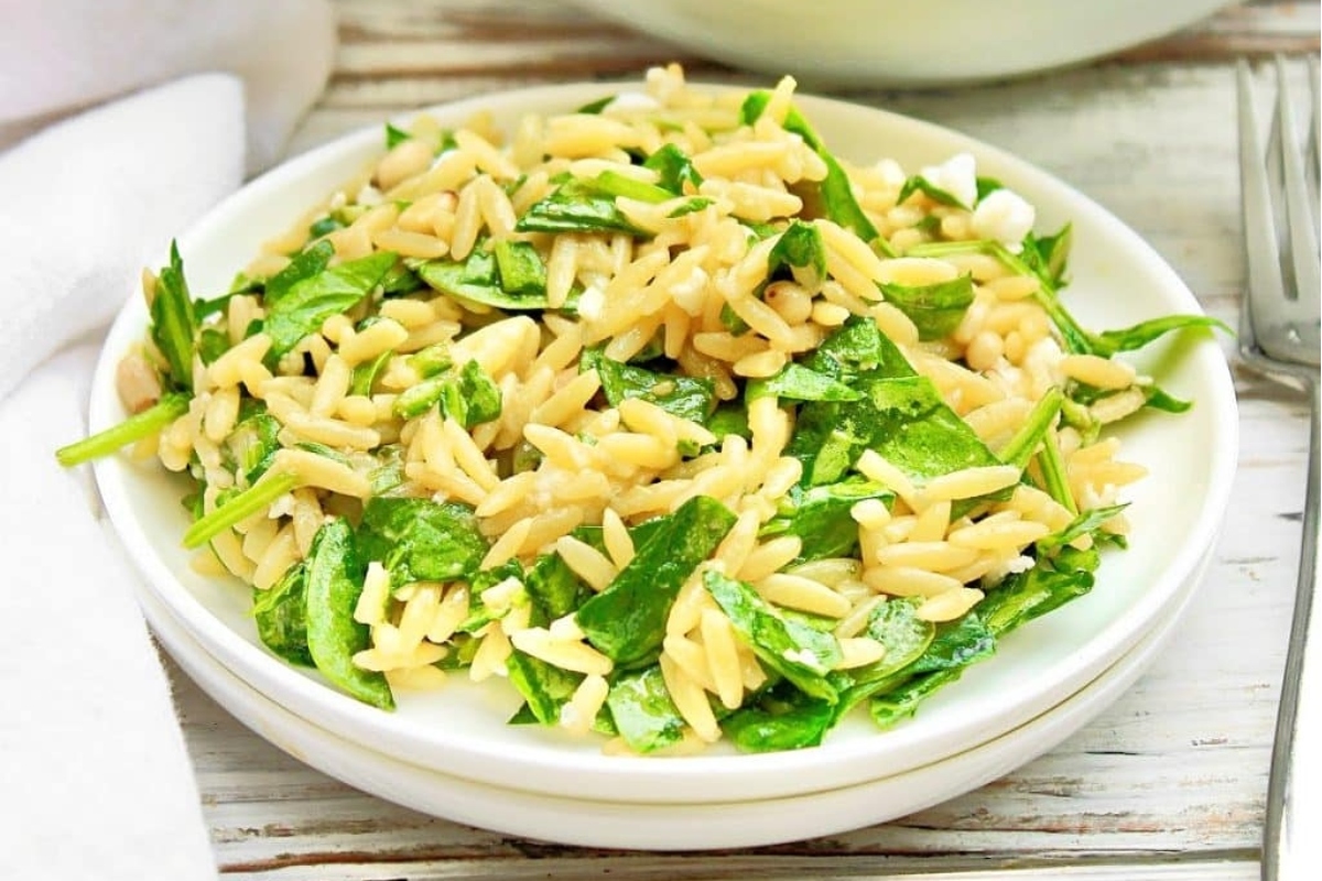 A bowl of spinach and orzo salad with a fork.