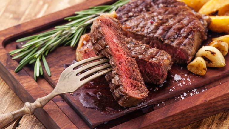 Sliced medium rare grilled Beef steak Ribeye with roasted potato wedges on cutting board on wooden background