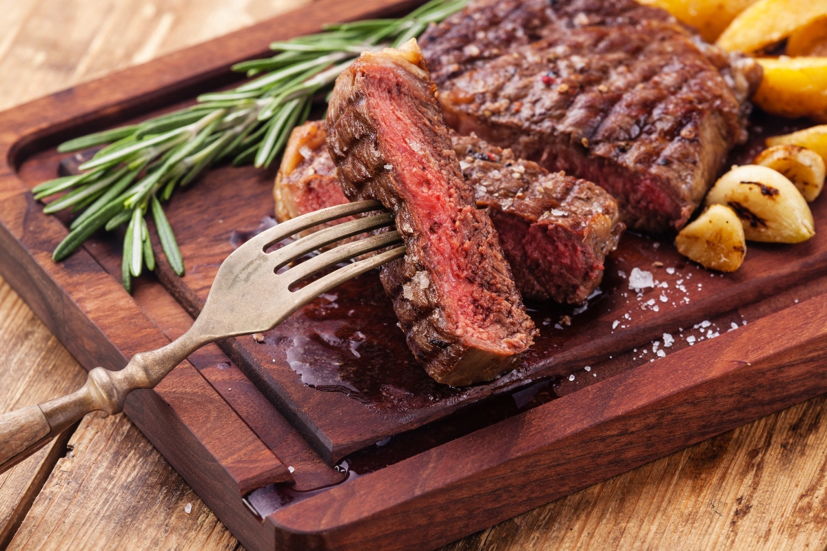 Sliced medium rare grilled Beef steak Ribeye with roasted potato wedges on cutting board on wooden background