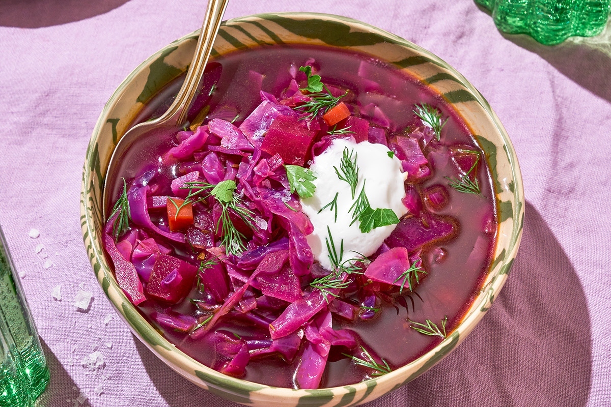 A bowl of red cabbage soup with sour cream.