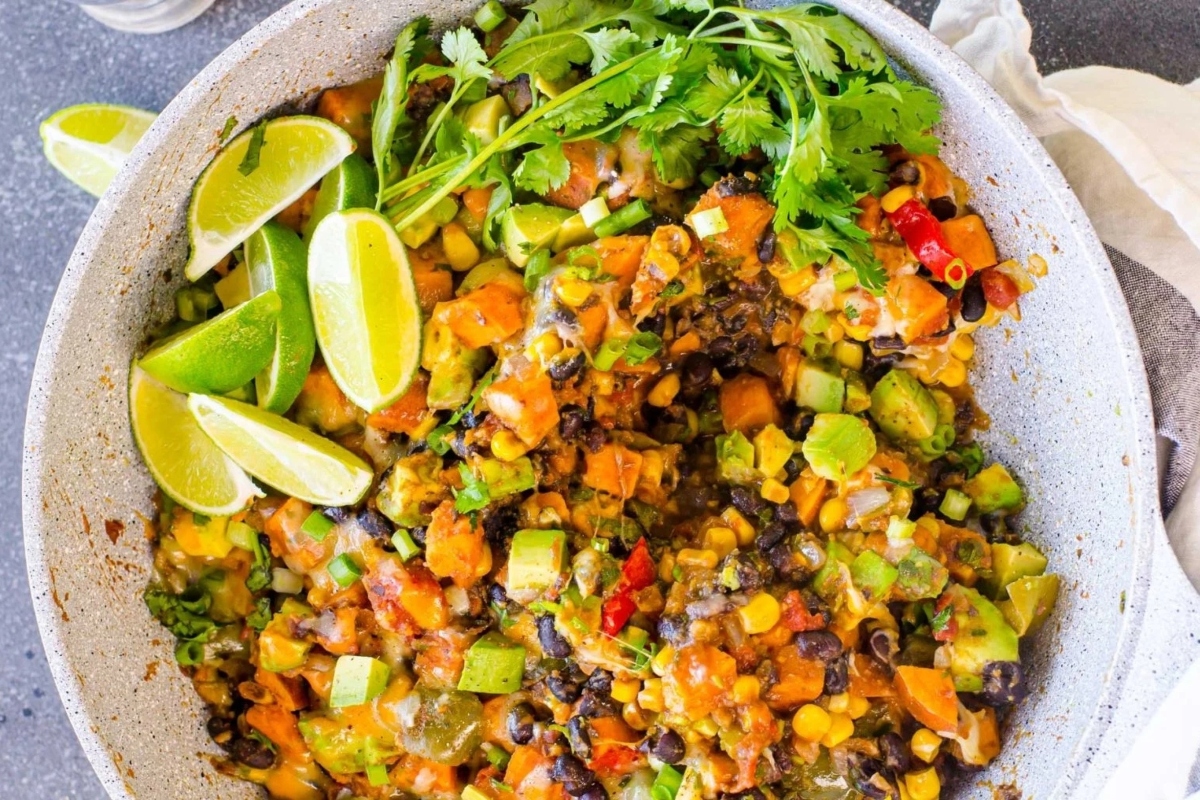 A bowl of black beans and sweet potatoes with lime wedges.