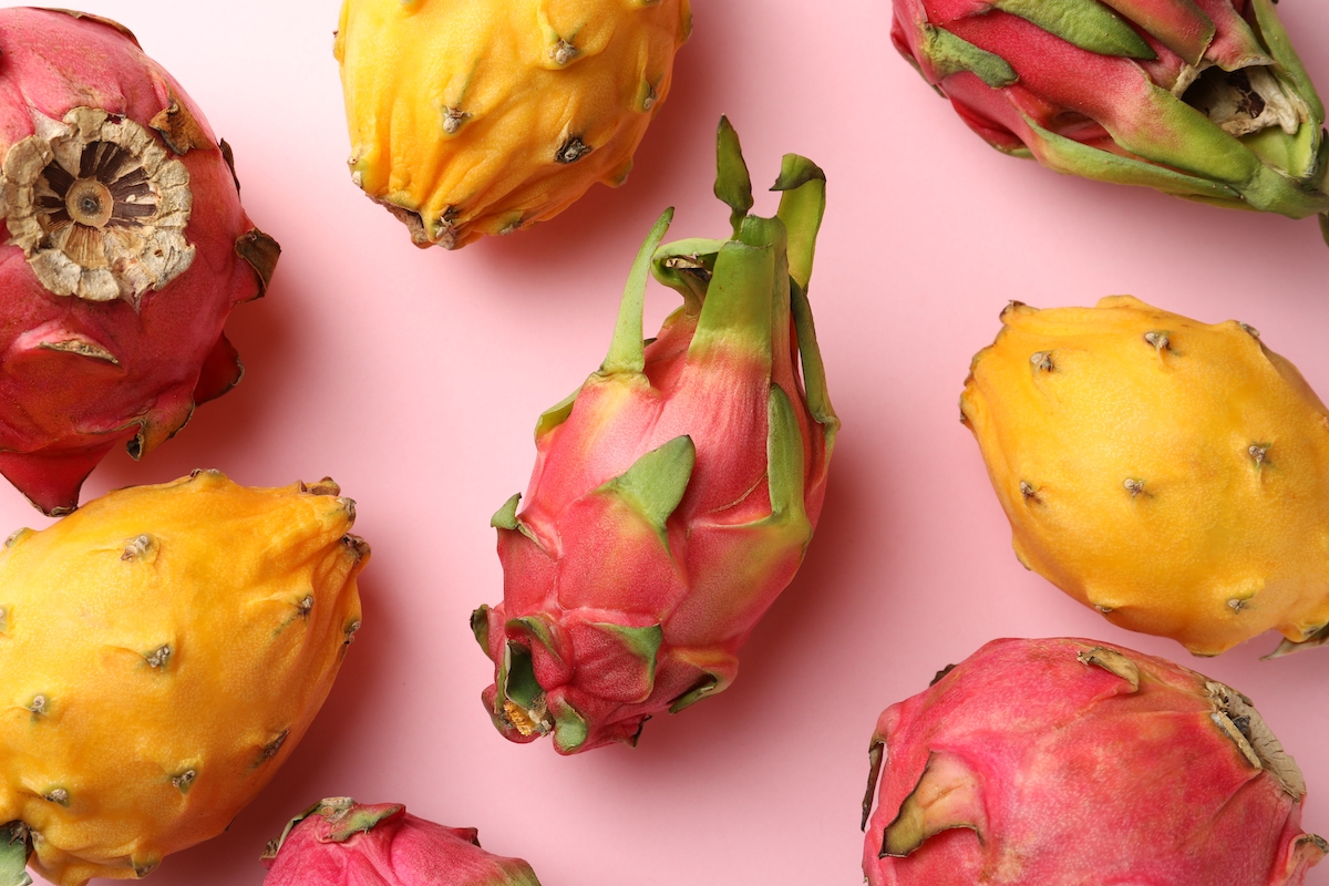 Different dragon fruits on light pink background, flat lay.